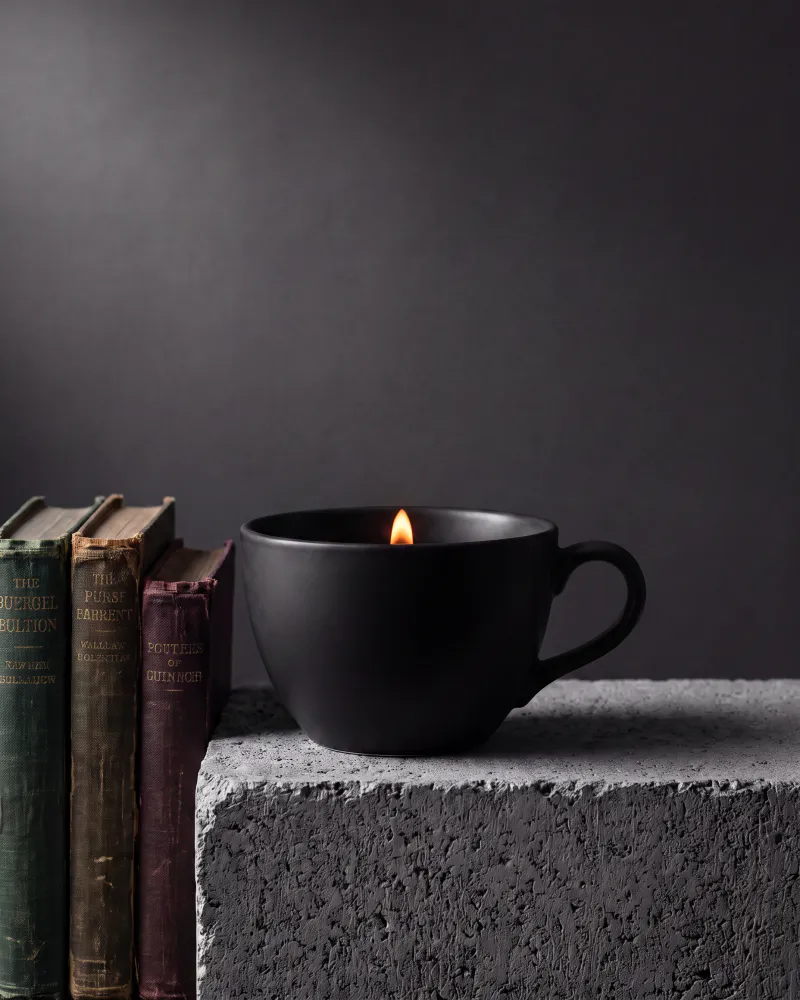Same camera, same lighting, same dark backdrop: a short stack of three weathered hardback books now stands beside the cup on the concrete plinth